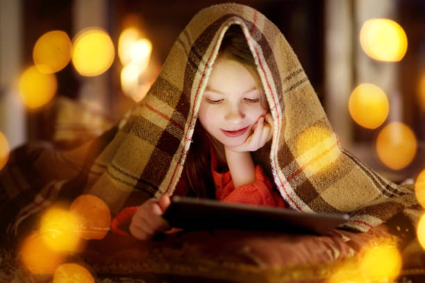 istock Adorable little girl using a tablet pc by a fireplace on Christmas evening 1057712502