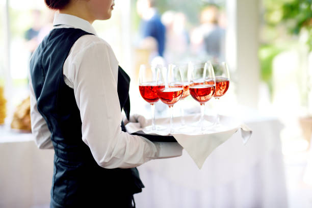 Waitress holding a dish of champagne and wine glasses at festive event Waitress holding a dish of champagne and wine glasses at festive event, party or wedding reception cafe transparent glass table stock pictures, royalty-free photos & images