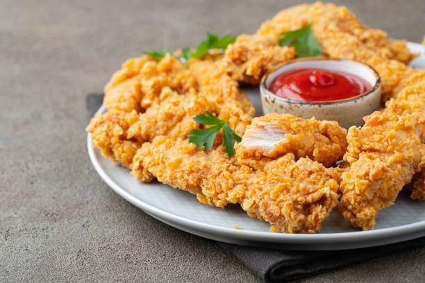 istock Breaded chicken strips with tomato ketchup on a white plate. Fast food on dark brown background 1057728682