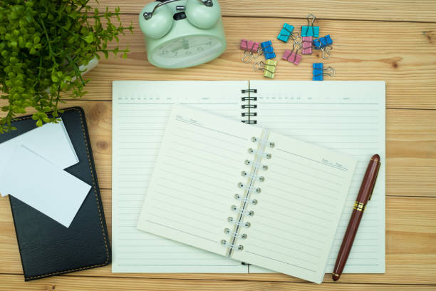 istock Office supplies or office work essential tools items on wooden desk in workplace, pen with notebook and alarm clock, top view 1057734834