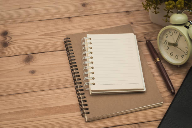 istock Office supplies or office work essential tools items on wooden desk in workplace, pen with notebook and alarm clock. 1057734854