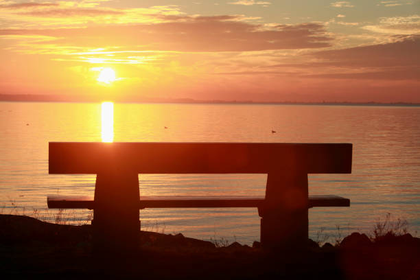 Landscape of Park Bench in Silhouette with Ocean and mountains at Sunset.