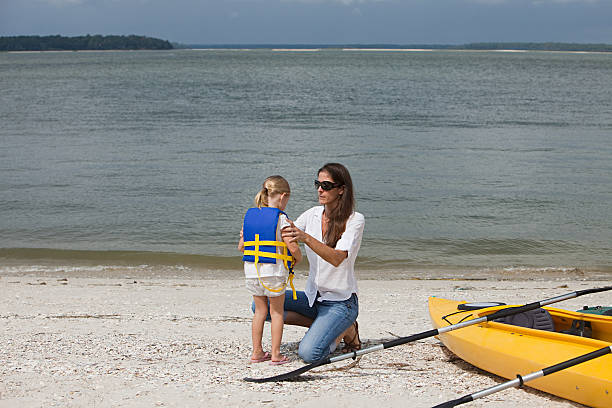 мать, делая жизнь жакет на дочь на каяках - women kayaking life jacket kayak стоковые фото и изображения