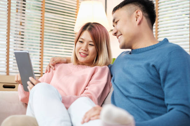 istock Asian couple watching video live on tablet on sofa in living room at home.lover spending time together. 1057788198