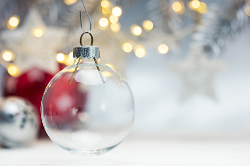 blurred grey background with glowing garlands and fir branch, focus on glass christmas ball