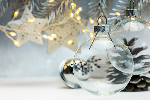 christmas glass balls hanging against grey background with blurred garland lights and fir branches