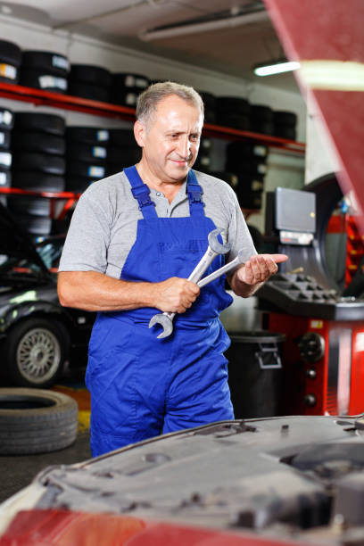istock Pensive elderly man mechanic looking at car in auto workshop, determining scope of work 1057815094