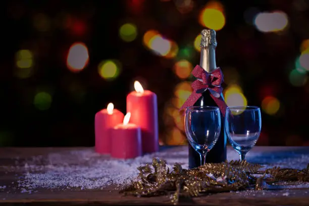 Image of a champagne bottle and burning candles on the table with blurred Christmas light background