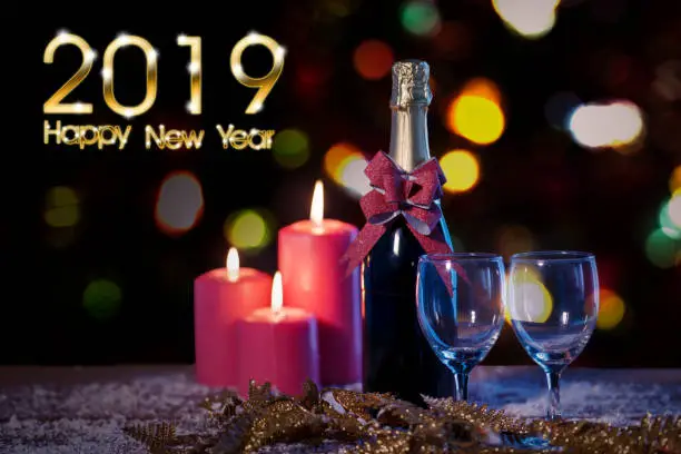 Image of a Champagne bottle and burning candles on the table with shiny 2019 Happy New Year text