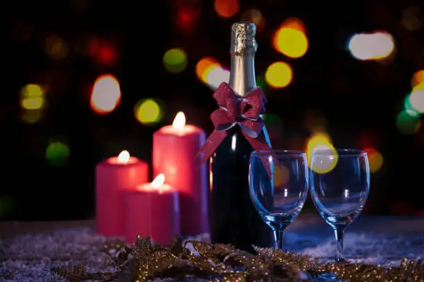 Christmas candles and champagne bottle over snow with blurred sparkling light background
