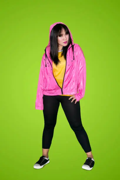 Beautiful woman in a pink jacket with hood while standing in the studio with green screen