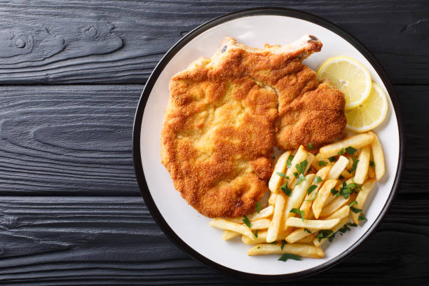 Traditional Italian veal Milanese with lemon and French fries close-up. horizontal top view Traditional Italian veal Milanese with lemon and French fries close-up on a plate. horizontal top view from above schnitzel stock pictures, royalty-free photos & images