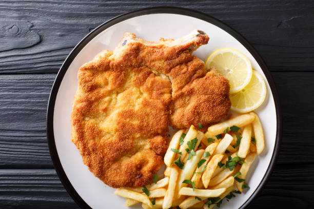 Fried veal cutlet Milanese with lemon and French fries close-up. horizontal top view Fried veal cutlet Milanese with lemon and French fries close-up on a plate. horizontal top view from above scaloppini stock pictures, royalty-free photos & images
