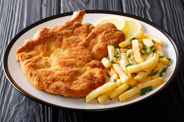 Fried veal cutlet Milanese with lemon and French fries close-up on a plate. Horizontal Fried veal cutlet Milanese with lemon and French fries close-up on a plate on a table. Horizontal schnitzel stock pictures, royalty-free photos & images