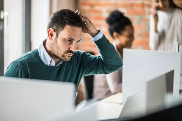 Photo of Young worried businessman working on laptop at corporate office.