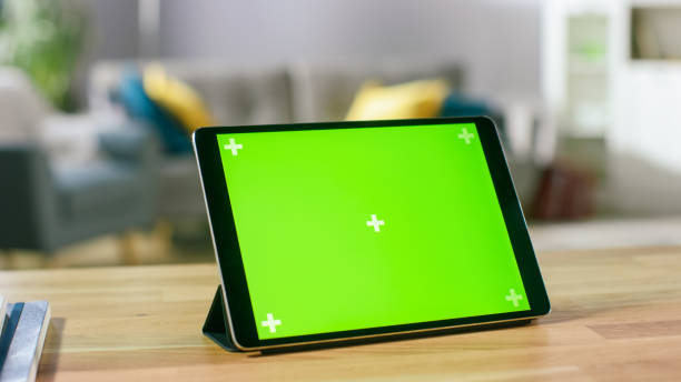 ランドス ケープ モードでの机の上に立っている緑モックアップ画面デジタル タブレット コンピューターの移動撮影。フィールド居心地の良いリビング ルームの背景の深さ。 - ipad digital tablet computer monitor blank ストックフォトと画像