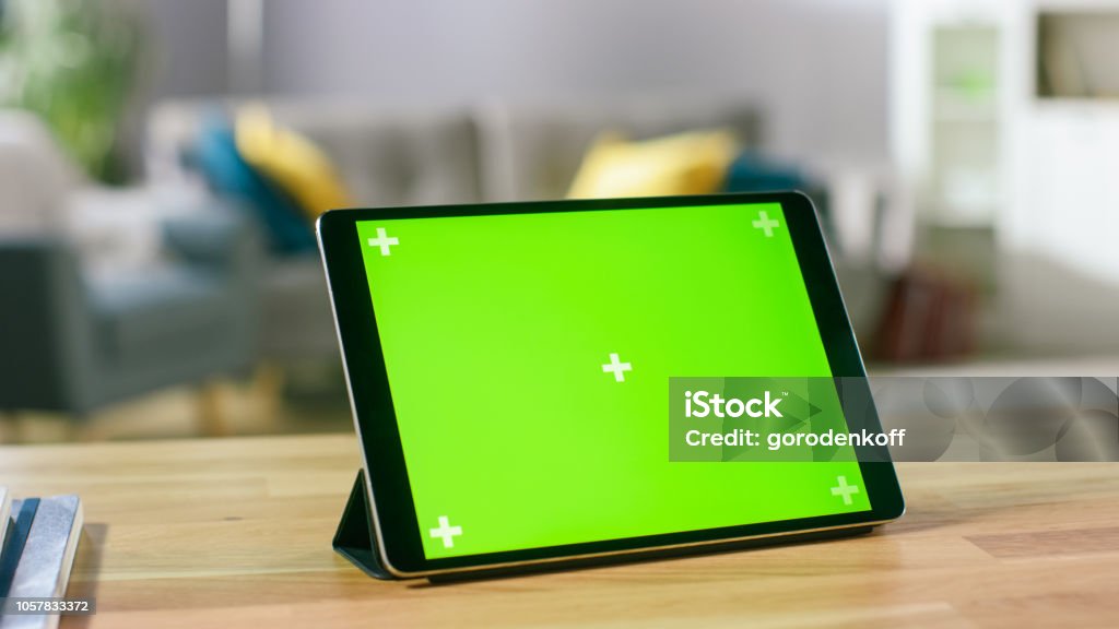 Moving Shot of the Green Mock-up Screen Digital Tablet Computer Standing on a Desk in Landscape Mode. In the Background Depth of Field Cozy Living Room. Digital Tablet Stock Photo