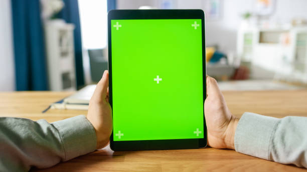 istock First Person Shot of Man Using Green Mock-up Screen Digital Tablet Computer in Portrait Mode while Sitting at His Desk. In the Background Cozy Living Room. 1057833378