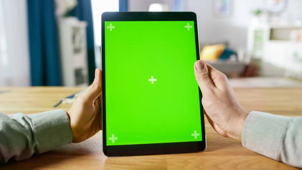 istock First Person Shot of a Man Using Hand Gestures on Green Mock-up Screen Digital Tablet Computer in Portrait Mode while Sitting at His Desk. In the Background Cozy Living Room. 1057833400