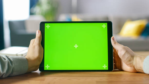 istock Close-up of Man Using Green Mock-up Screen Digital Tablet Computer in Landscape Mode while Sitting at His Desk. In the Background Cozy Living Room. 1057833454