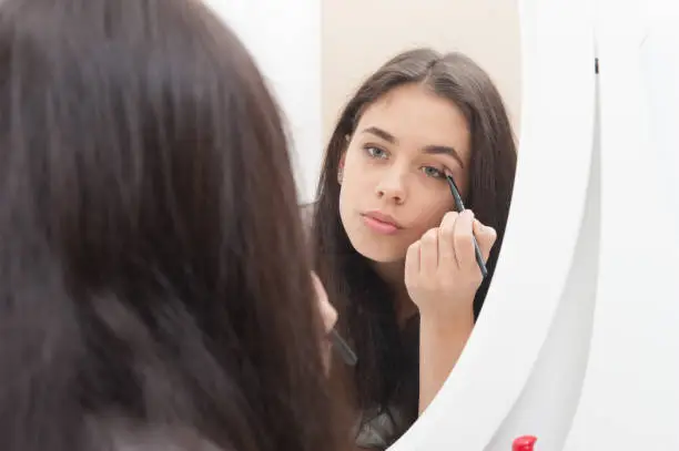 The girl applies makeup and looks in the dressing-table mirror