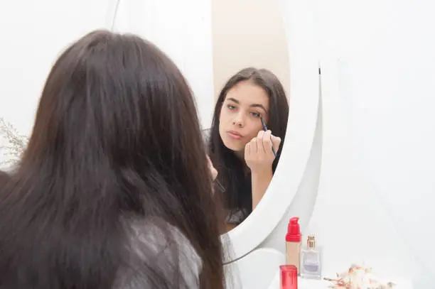 The girl applies makeup and looks in the dressing-table mirror
