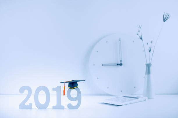istock 2019 study abroad program, time schedule arrangement, education concept : Black graduation cap on year 2019 wood cut, calculator, white plain clock at 9 o'clock on desk table. Light white, clean theme 1057856968