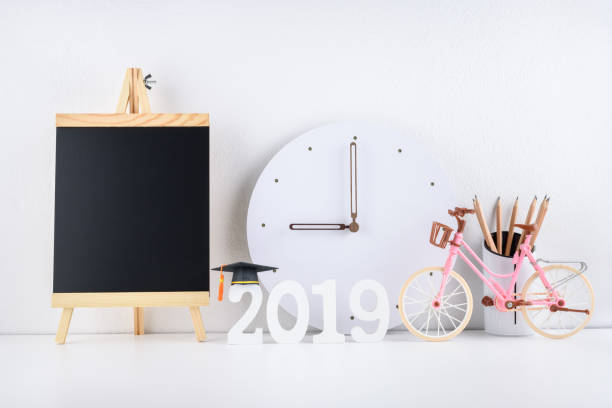 istock 2019 happy new year / graduate study abroad program, time schedule arrangement, education concept : Black graduation cap of success on number 2019 white wood cut, clock on student desk, office table 1057856978