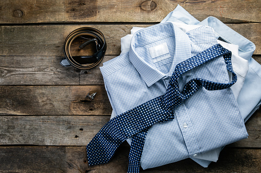 Selection of male clothes - stack of folded shirts, tie, belt, cufflinks, rustic wood background