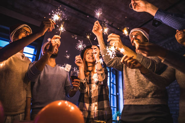 Below view of happy colleagues using sparklers while celebrating New Year in the office. Low angle view of large group of happy colleagues using sparklers on Christmas party. New Year’s Eve Outfit stock pictures, royalty-free photos & images