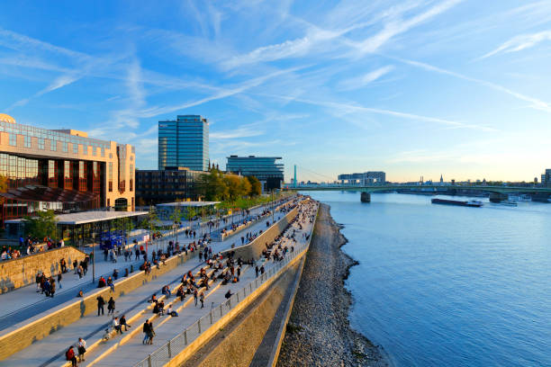 Cologne, Germany - October 21, 2018. Tourists and natives on the brand new river rhine promenade and staircase opposite to the old town of Cologne. Skyline of renewed office buildings, the three crane buildings and the Severin bridge in the background.