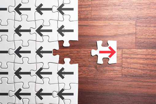 Jigsaw puzzle piece with red arrow facing the opposite direction from crowd.