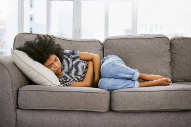 These cramps are a killer Shot of a young woman experiencing stomach pain on the sofa at home pms photos stock pictures, royalty-free photos & images