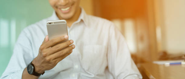 istock close up asian man hand holding smartphone for watching video streaming on device with smiling happiness after finish work at office , people relaxing time concept 1057895592