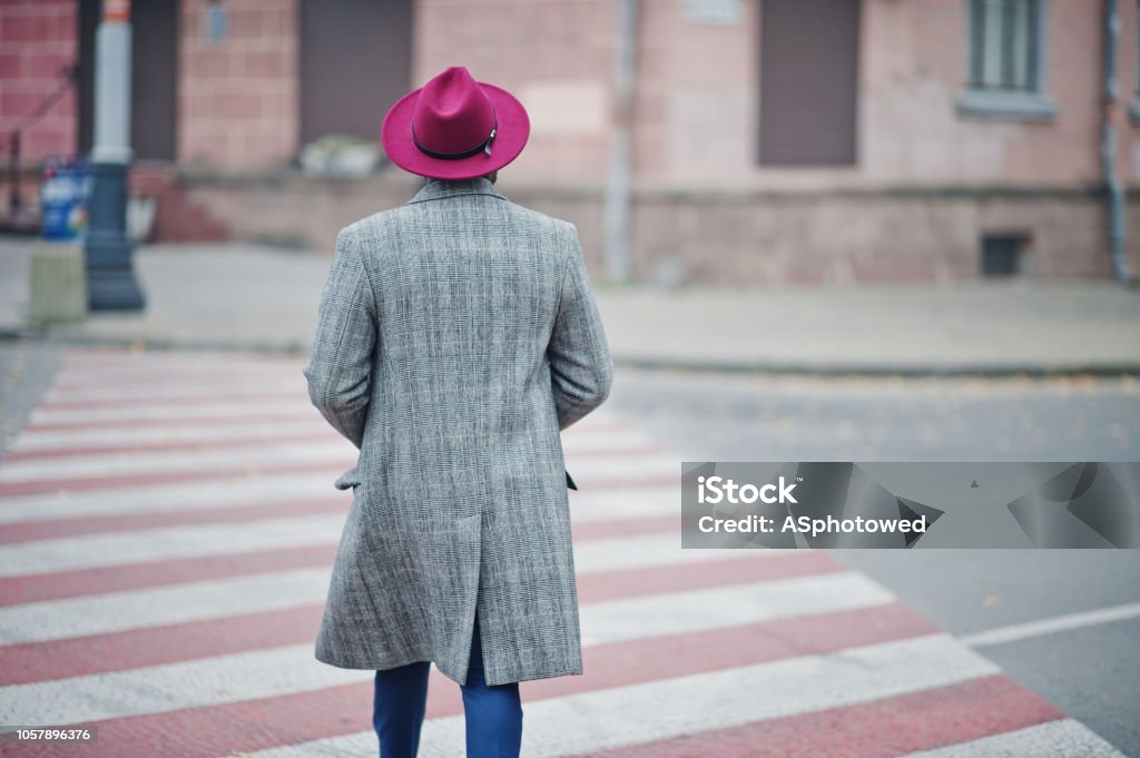 Stylish African American man model Back of walking stylish African American man model in gray coat and red hat at crosswalk. Adult Stock Photo