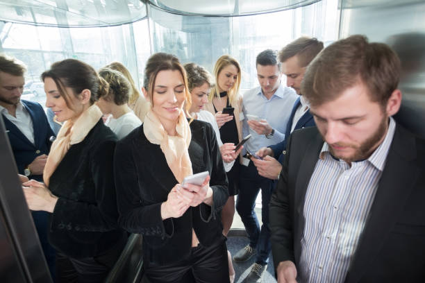 istock Business people using smart phones in glass elevator 1057912452