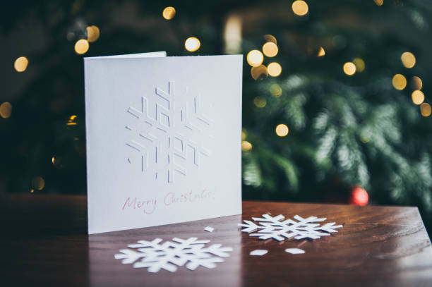 Embossed snowflake Christmas card displays on table against Christmas tree background
