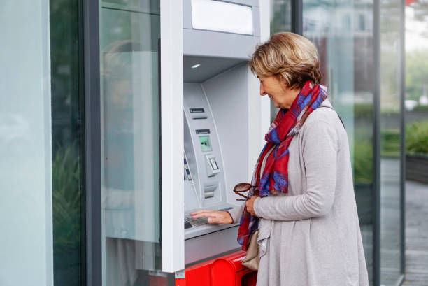 Senior woman using ATM in the city stock photo