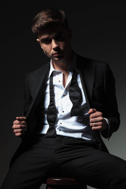 istock seductive man with undone bowtie holding tuxedo collar while sitting 1057921450