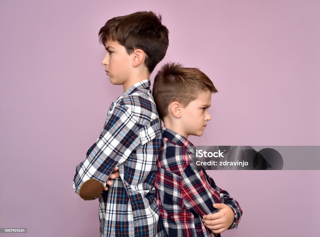 Two angry brothers standing back to back Two angry and frowning brothers standing back to back, not talking to each other Brother Stock Photo