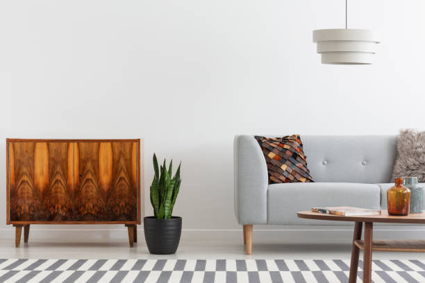 istock Plant between wooden cabinet and grey settee in white flat interior with lamp and table. Real photo 1057923752