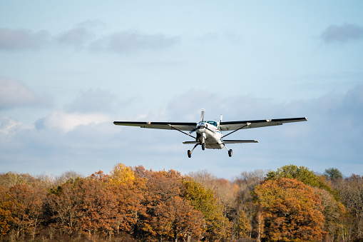 Small plane with single propeller taking of from the runway. Sunshine and autumn colored trees in the background