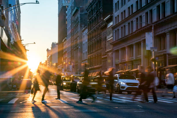 People crossing the street in Manhattan New York City Rays of sunlight shine on the busy people walking across an intersection in Midtown Manhattan in New York City NYC midtown manhattan photos stock pictures, royalty-free photos & images