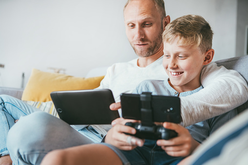 Father and son game players funs sit together using the tablet and gamepad at home on cozy sofa