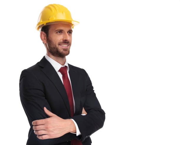 confident businessman wearing a yellow helmet looks up to side - businessman business arms crossed business person imagens e fotografias de stock