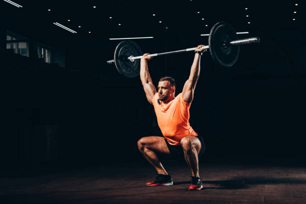 attractive athletic man working out with barbell in dark gym attractive athletic man working out with barbell in dark gym cross training stock pictures, royalty-free photos & images