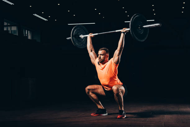 attractive athletic man working out with barbell in dark gym - crosstraining imagens e fotografias de stock