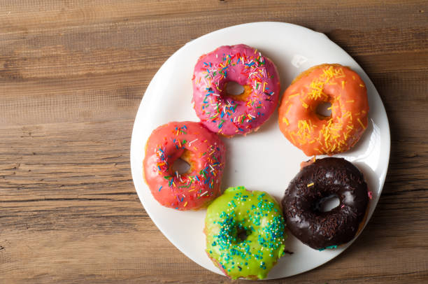 istock Multi-colored glazed donuts. On a white plate, on wooden boards. Coffee to donuts 1057946380