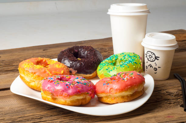 istock Multi-colored glazed donuts. On a white plate, on wooden boards. Coffee to donuts 1057946516