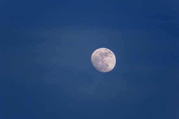istock Full moon in daytime in blue hour with soft white clouds 1057950700